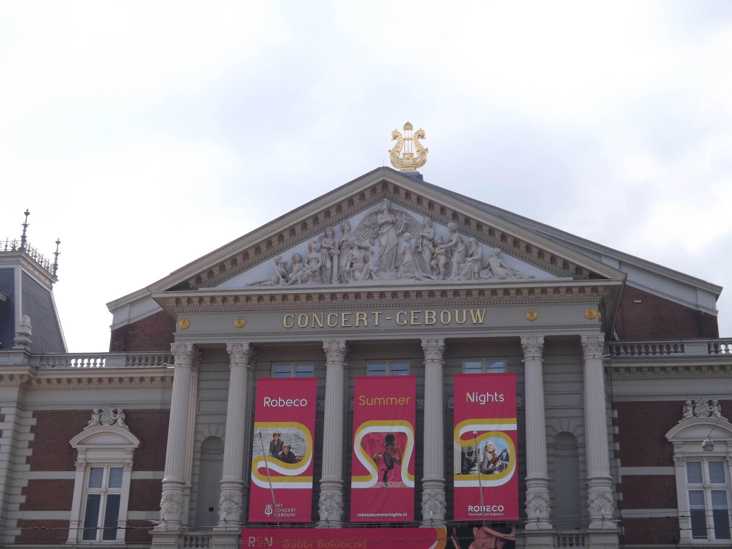 The Concertgebouw building with classical architecture and three red banners advertising events.