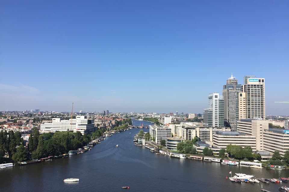 A river with boats, a city skyline, and a clear blue sky.