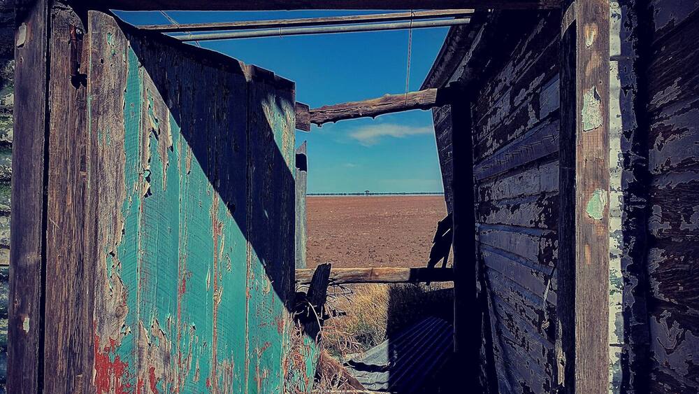 A dilapidated wooden structure with peeling paint and a view of a flat landscape.