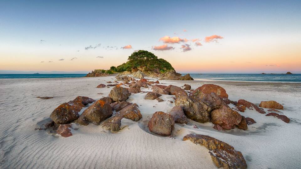 A beach with scattered rocks and a small island with trees in the distance.