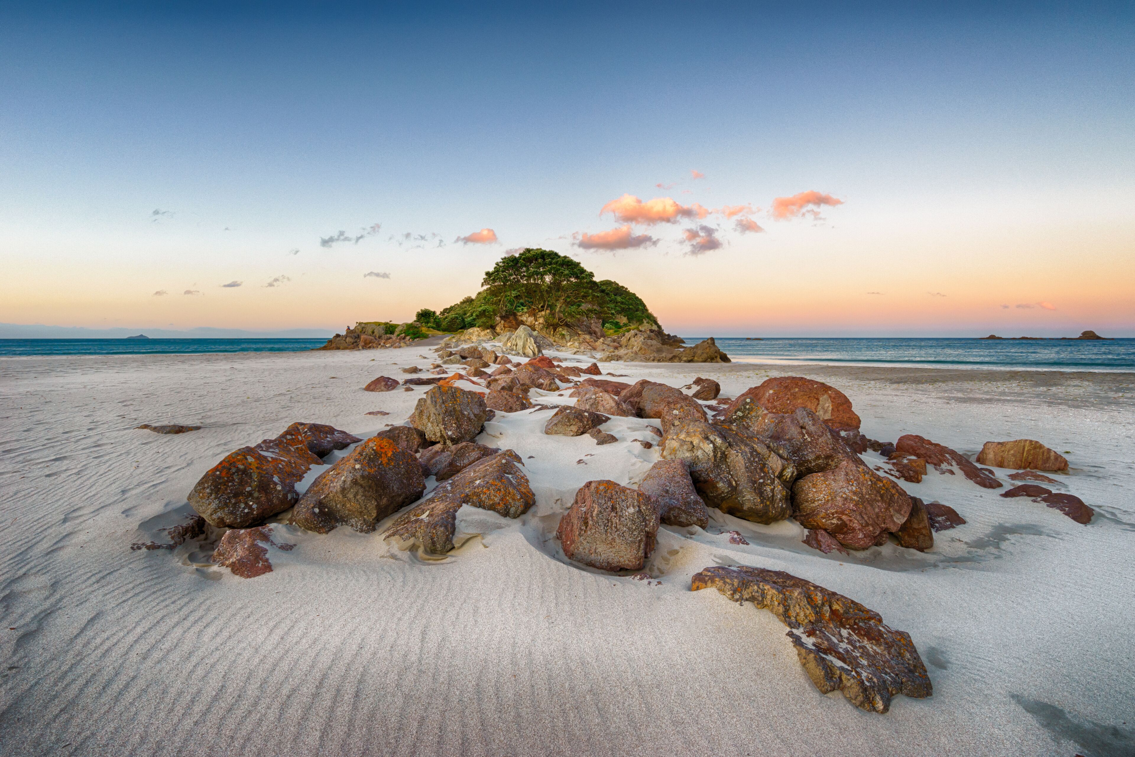 A beach with scattered rocks and a small island with trees in the distance.