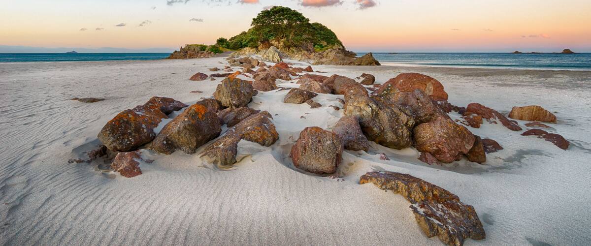 A beach with scattered rocks and a small island with trees in the distance.