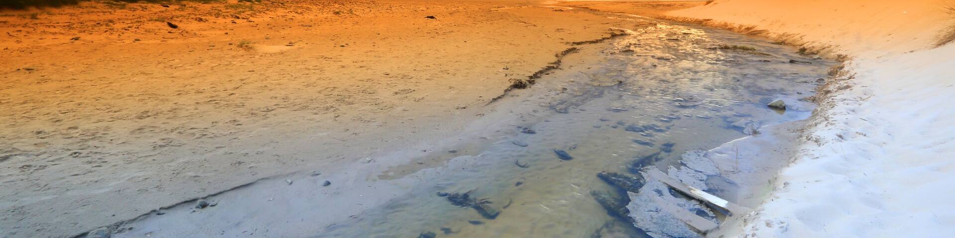 A beach with a sunset, sandy shore, and a cliff.
