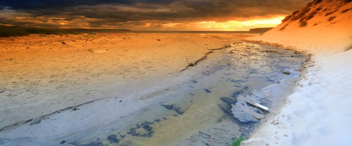 A beach with a sunset, sandy shore, and a cliff.