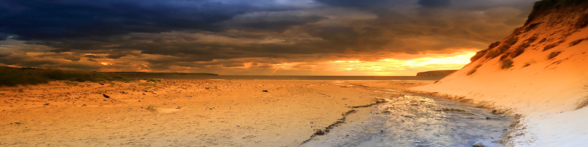 A beach with a sunset, sandy shore, and a cliff.