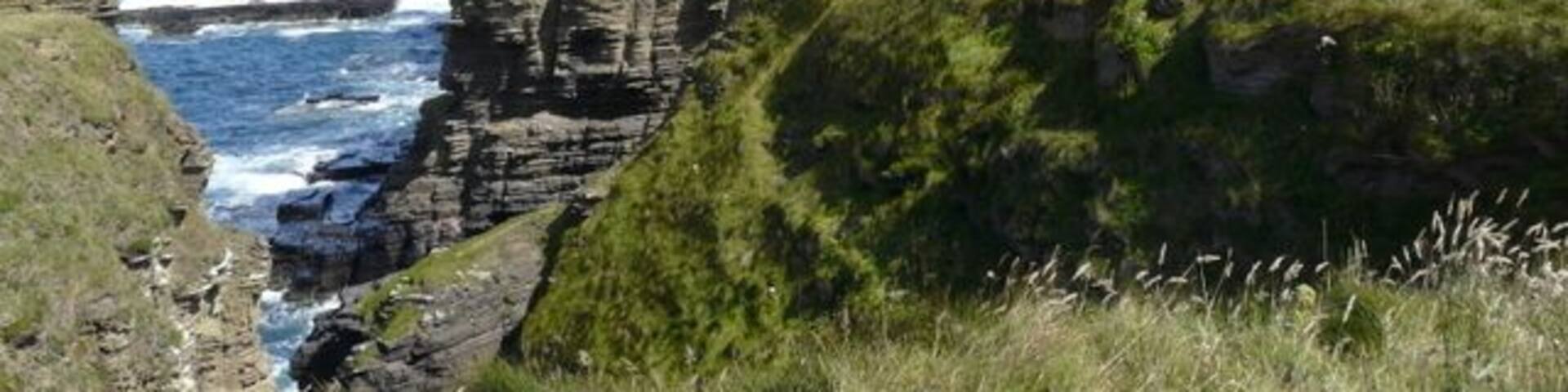 A coastal ruin with crumbling stone walls and a cliffside overlooking the ocean.