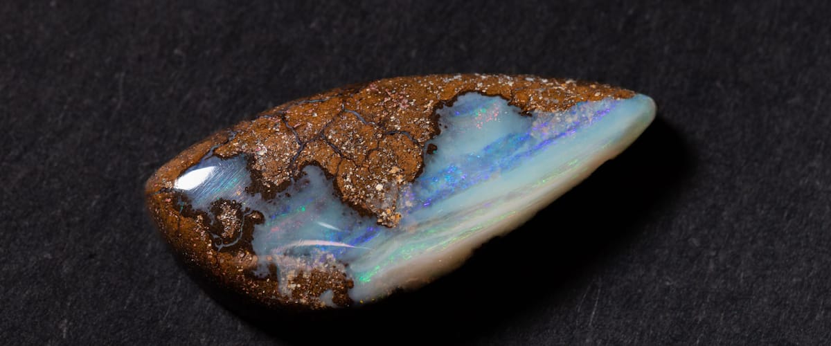 A polished opal gemstone with a brown exterior and iridescent blue and green interior.