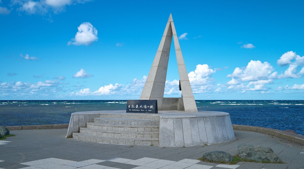 A monument with a sign in Japanese, located by the sea with a clear sky.