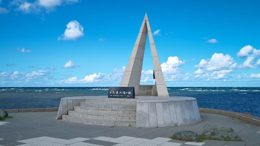 Un monumento con un cartel en japonés, situado junto al mar bajo un cielo despejado.