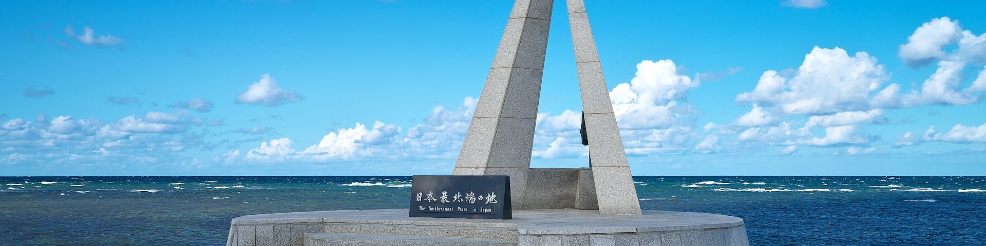 Un monumento con un cartel en japonés, situado junto al mar bajo un cielo despejado.