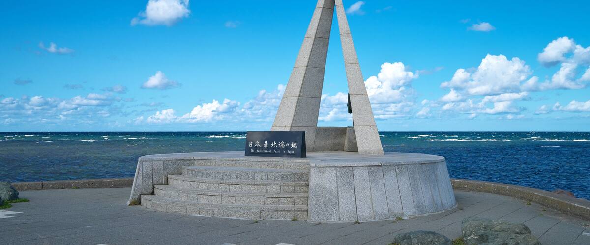 A monument with a sign in Japanese, located by the sea with a clear sky.