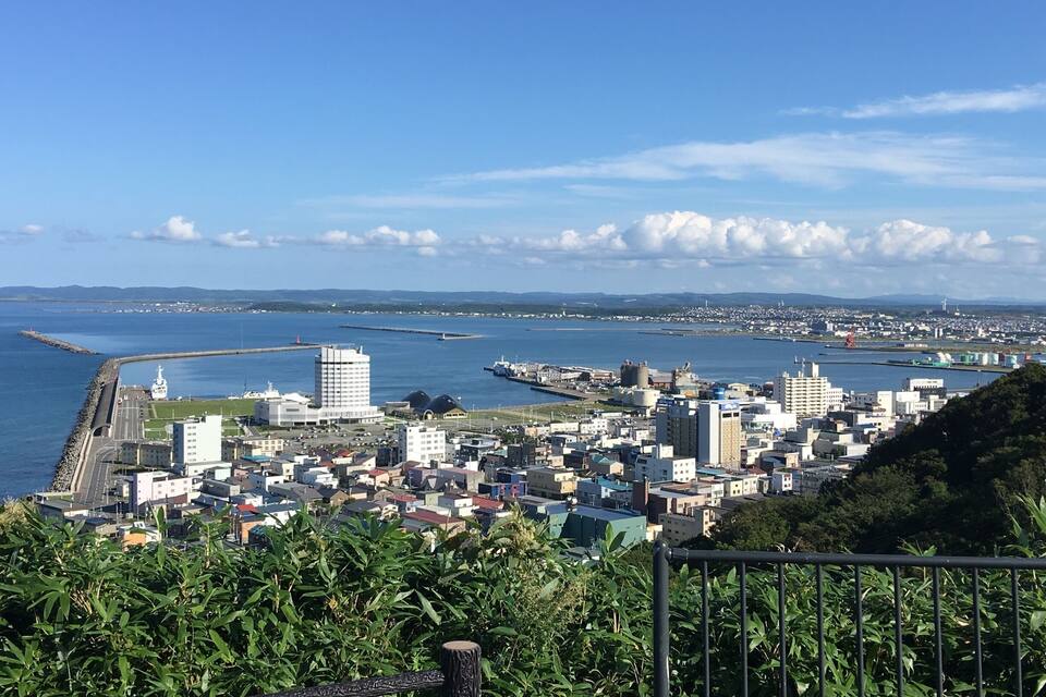 A coastal cityscape with a prominent lighthouse, a large white building, and a dense urban area with various structures.