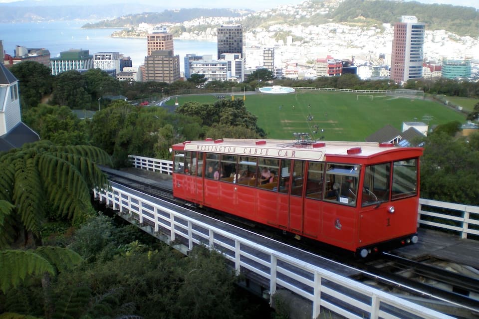 A red Wellington Cable Car traveling over a bridge with a cityscape in the background.