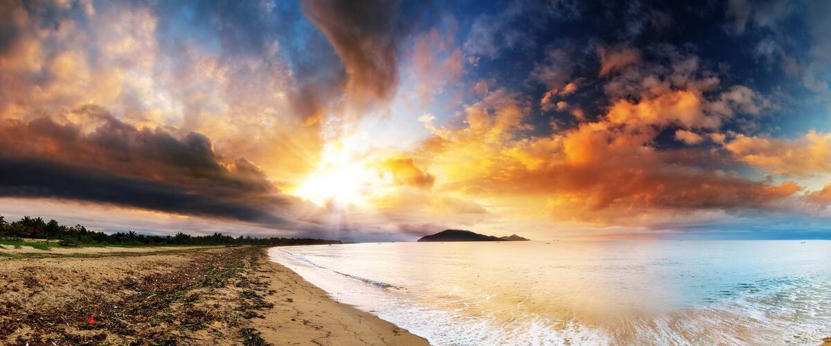 A beach with a sunset, calm sea, and scattered debris.