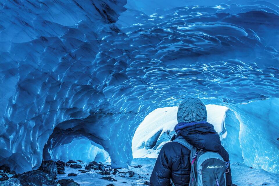 En person står foran en stor blå isgrotte.