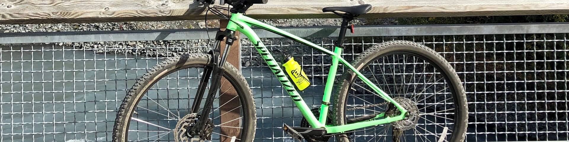 A green mountain bike parked on a wooden railing overlooking a river and mountains.