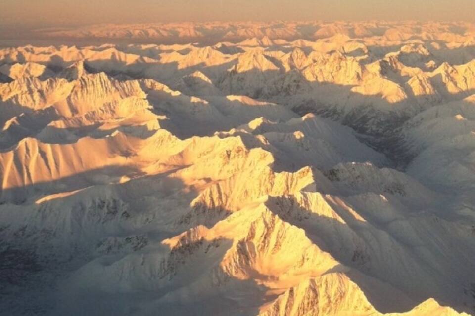 Ein weites, mit Schnee bedecktes Bergmassiv, das im warmen Sonnenlicht erstrahlt.