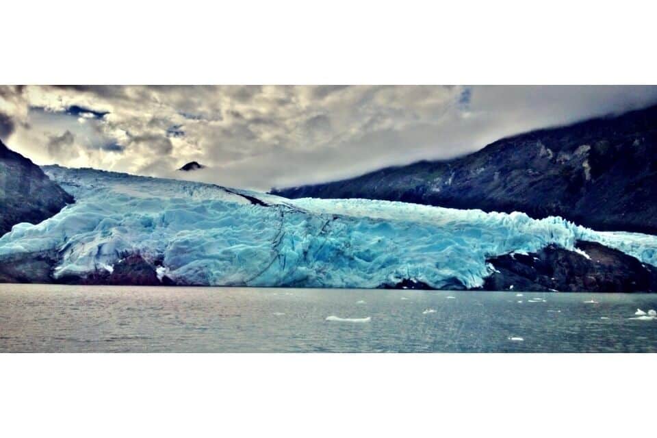 A glacier calving into a body of water with mountains in the background.