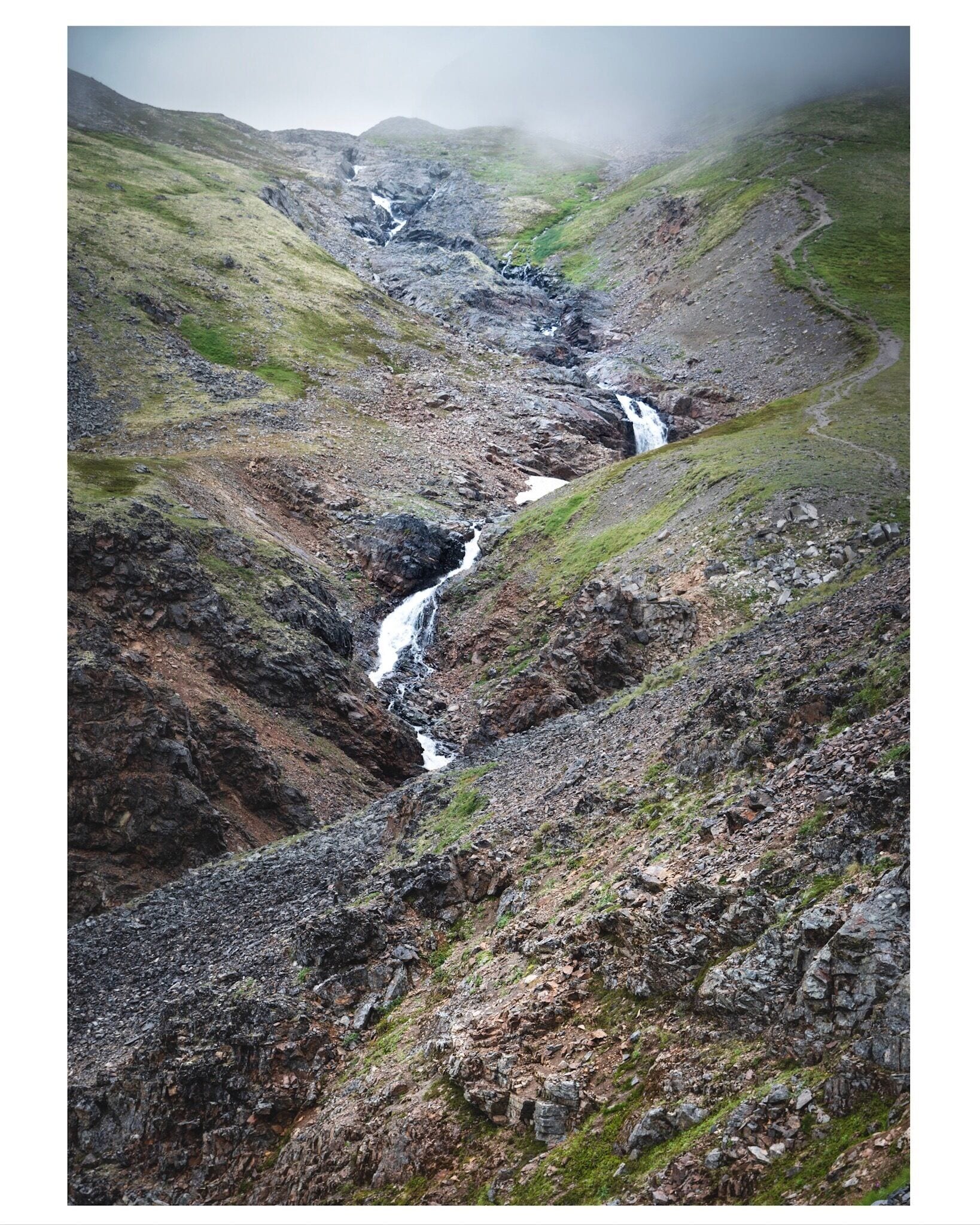 A mountainous landscape with a waterfall cascading down a rocky valley.