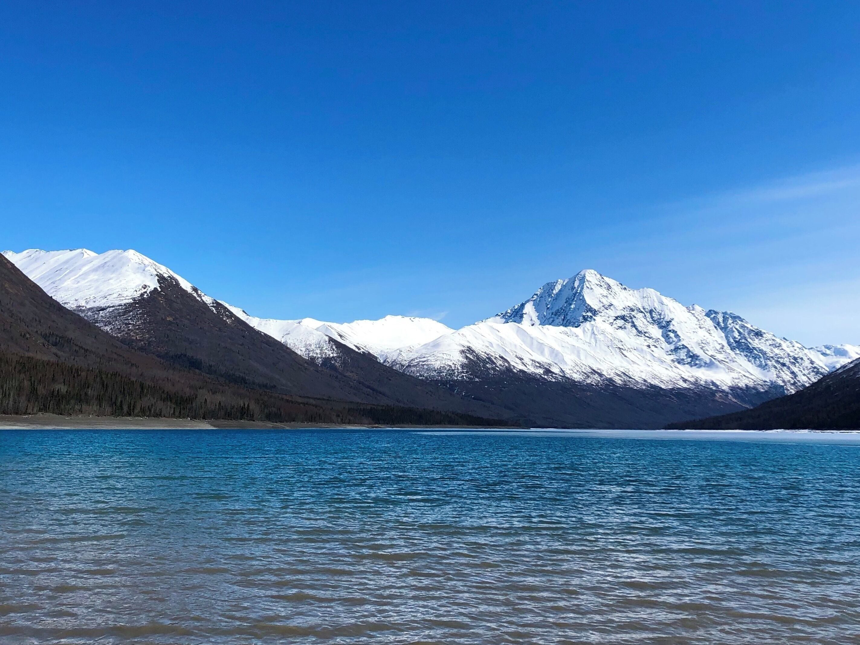 Um lago calmo com montanhas cobertas de neve ao fundo.