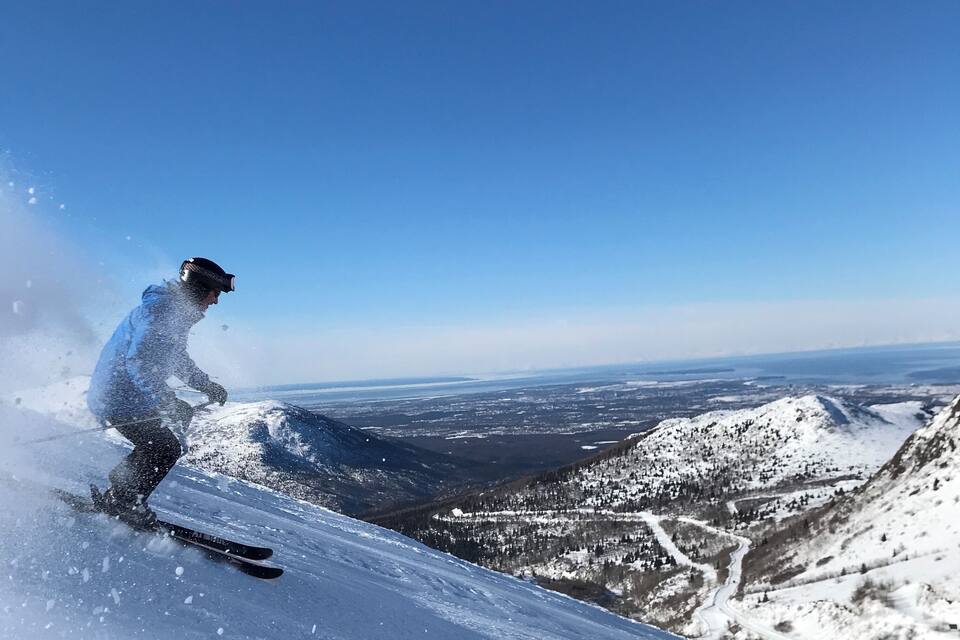 A skier on a snowy slope with a clear blue sky and distant mountains.