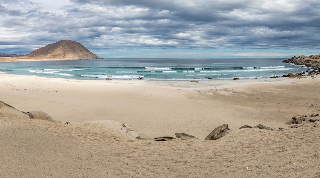 An idyllic beach at a remote location inside an arid landscape at Atacama Desert coast. The waves coming from the Pacific Ocean crash the rocks of the desert on an amazing wild dry scenery