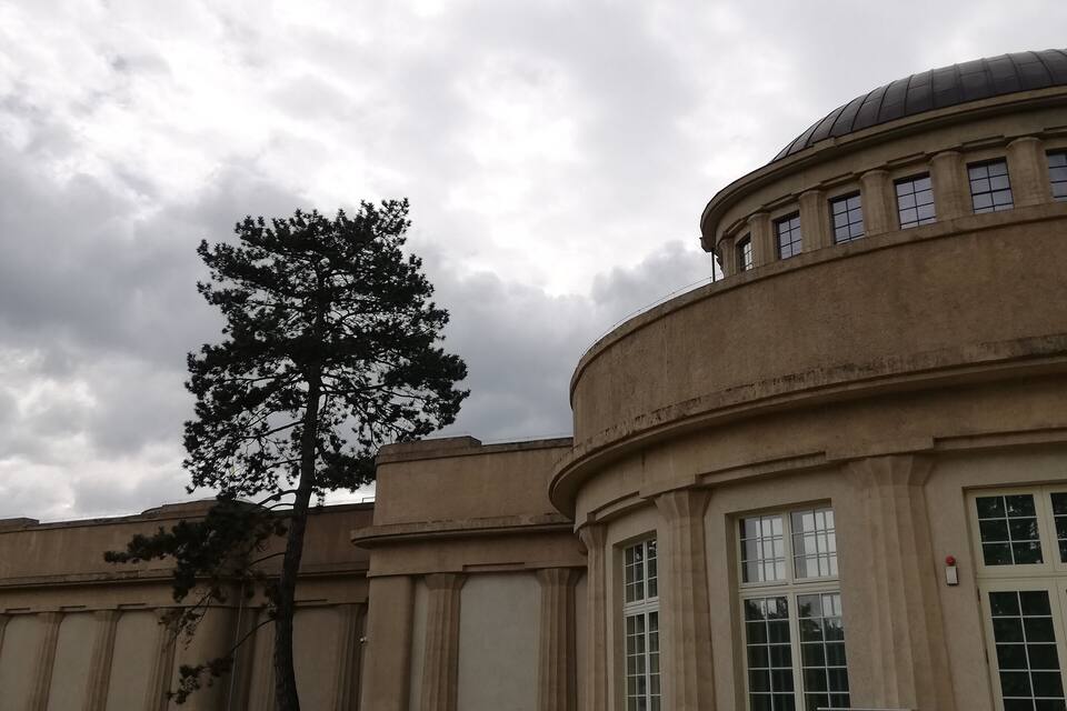 Un edifici gran amb una cúpula i columnes, envoltat d'un camí de grava i un arbre.