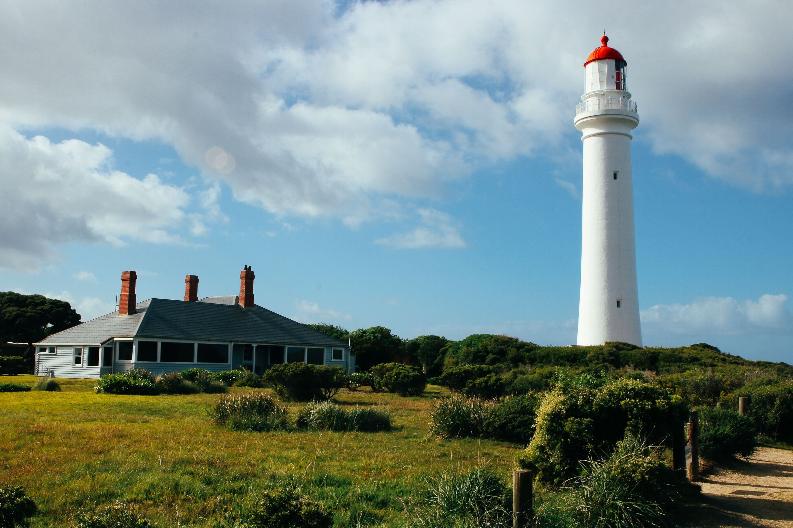 Split Point Lighthouse, Aireys Inlet, Victoria. Scenic landscape of lighthouse and caretaker's cottage in leafy green foliage amidst blue sky. 