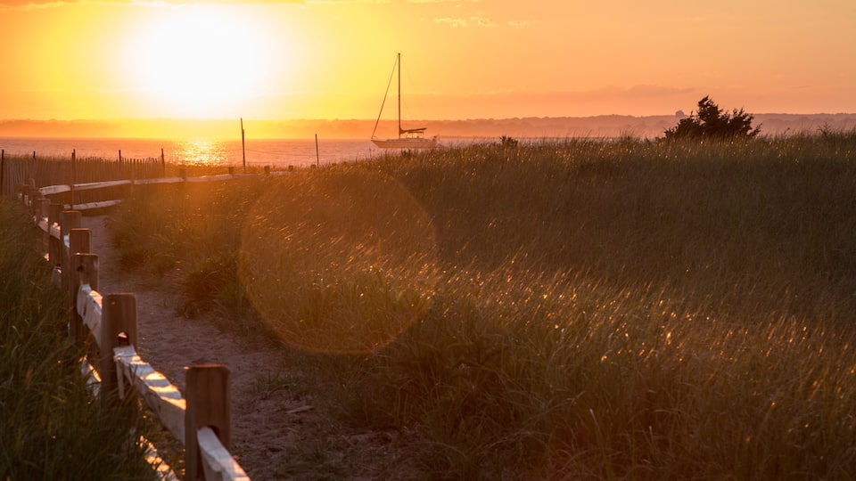 Beach path, wooden fence and sailboat at sunset at Napatree Point, Watch Hill, Westerly, Rhode Island, USA