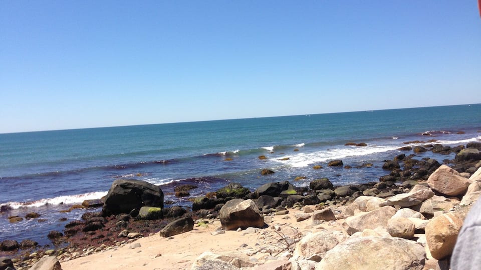 Una playa rocosa con olas rompiendo en la orilla bajo un cielo azul despejado.
