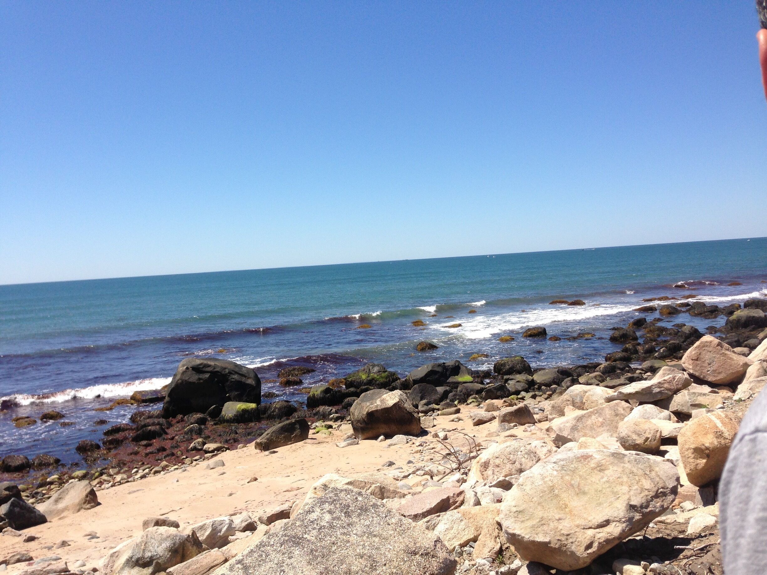 A rocky beach with waves crashing against the shore under a clear blue sky.