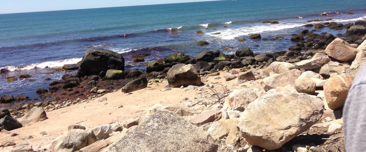 A rocky beach with waves crashing against the shore under a clear blue sky.
