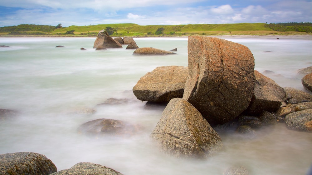 A coastal landscape with large boulders in the foreground and a calm sea.