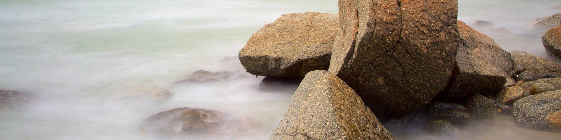 A coastal landscape with large boulders in the foreground and a calm sea.