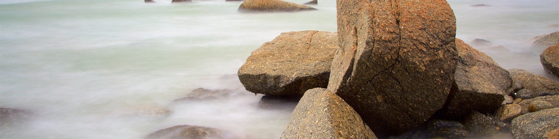 Un paisaje costero con grandes rocas en primer plano y un mar tranquilo.