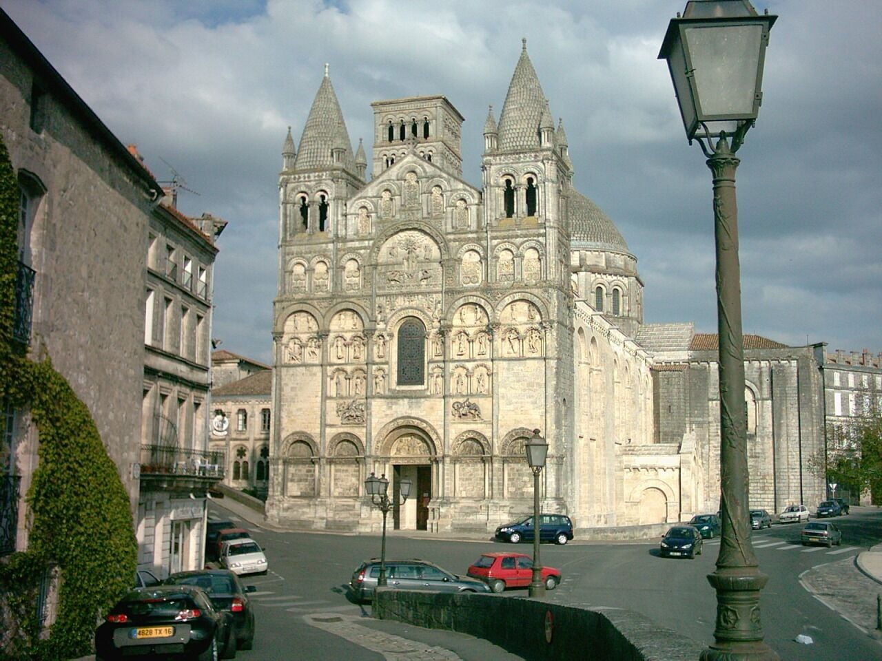 A historic cathedral with two towers, a street with cars, and a lamppost.