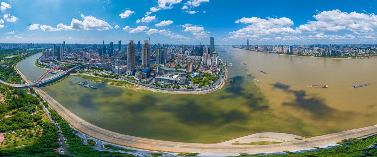 A panoramic view of a river with a cityscape, including high-rise buildings and a bridge.
