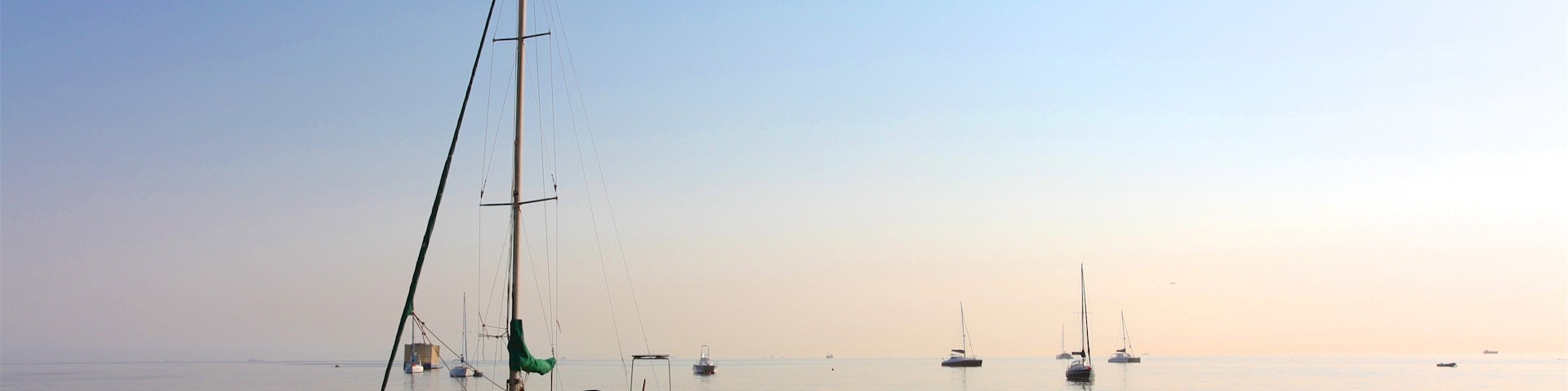 A calm sea with a sailboat anchored in the foreground and several other boats in the distance under a clear sky.