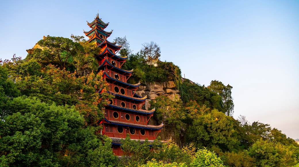 A traditional multi-tiered pagoda with ornate roofs, nestled among lush greenery and perched on a rocky cliff.