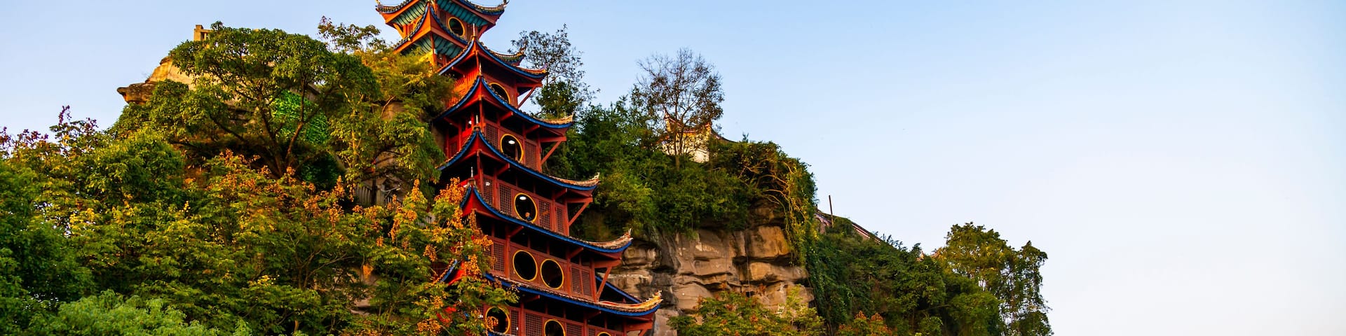 A traditional multi-tiered pagoda with ornate roofs, nestled among lush greenery and perched on a rocky cliff.