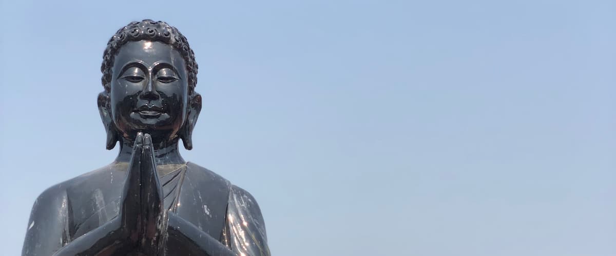 A black statue of a figure with hands in a prayer position, standing in front of a larger golden statue.
