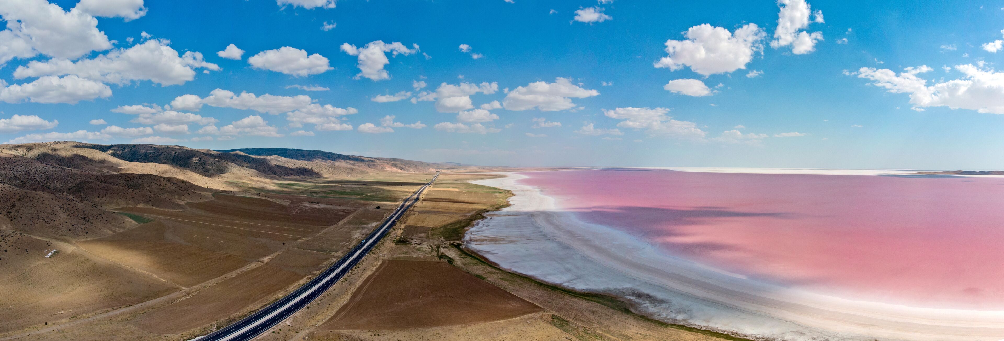 Una carretera serpentea por un paisaje desértico con un lago de color rosa llamativo.