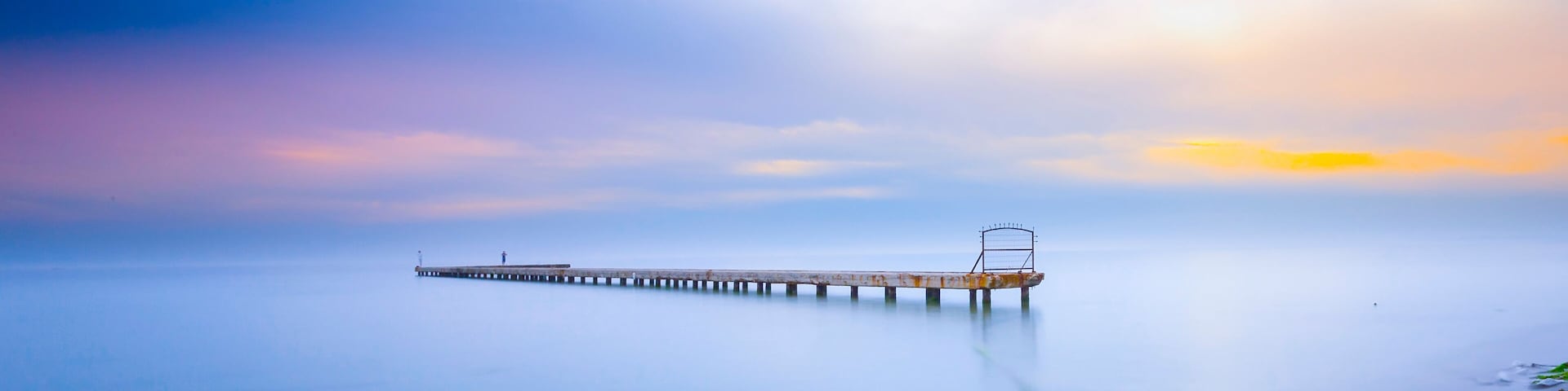 Eine Pier, die sich in ruhiges Wasser erstreckt, mit blauem Himmel darüber.