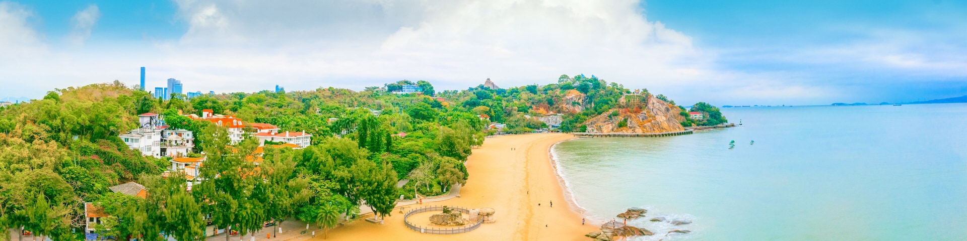 Paisagem costeira com uma praia arenosa, céu azul claro e uma grande nuvem.