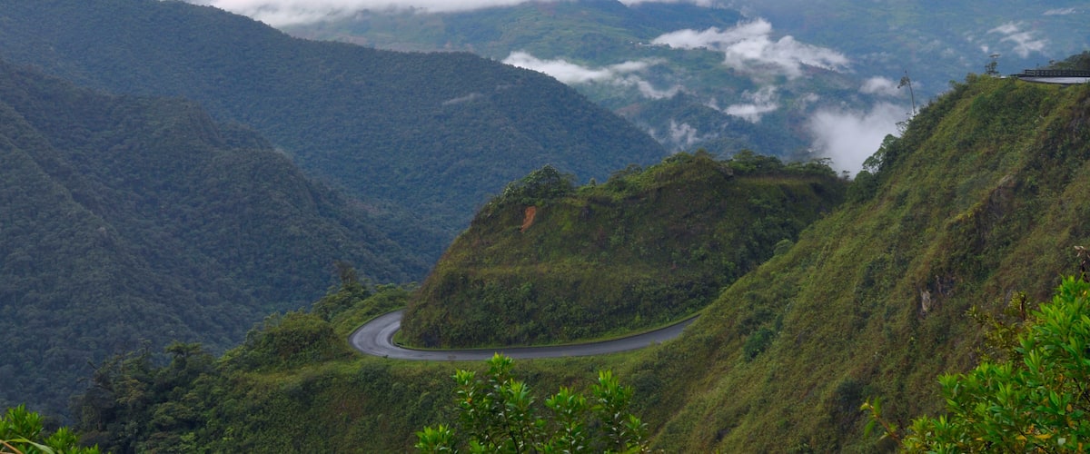 A winding road through a mountainous landscape with lush greenery and clouds below.