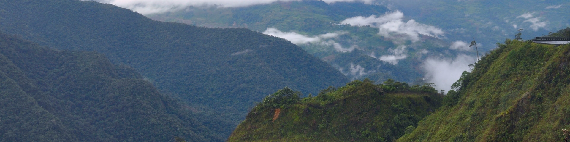 A winding road through a mountainous landscape with lush greenery and clouds below.