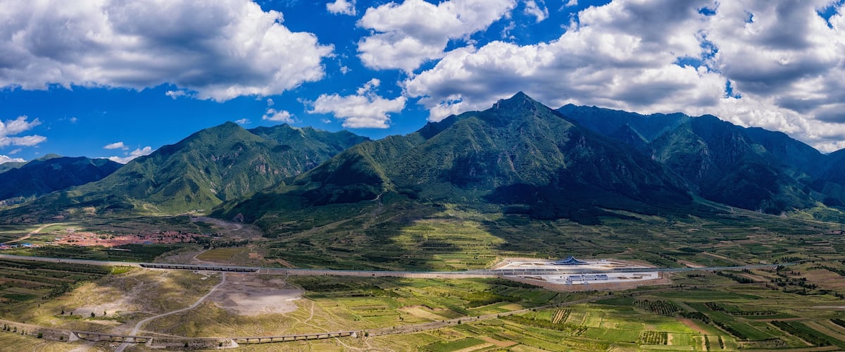 A mountainous landscape with a train track and a large industrial facility.