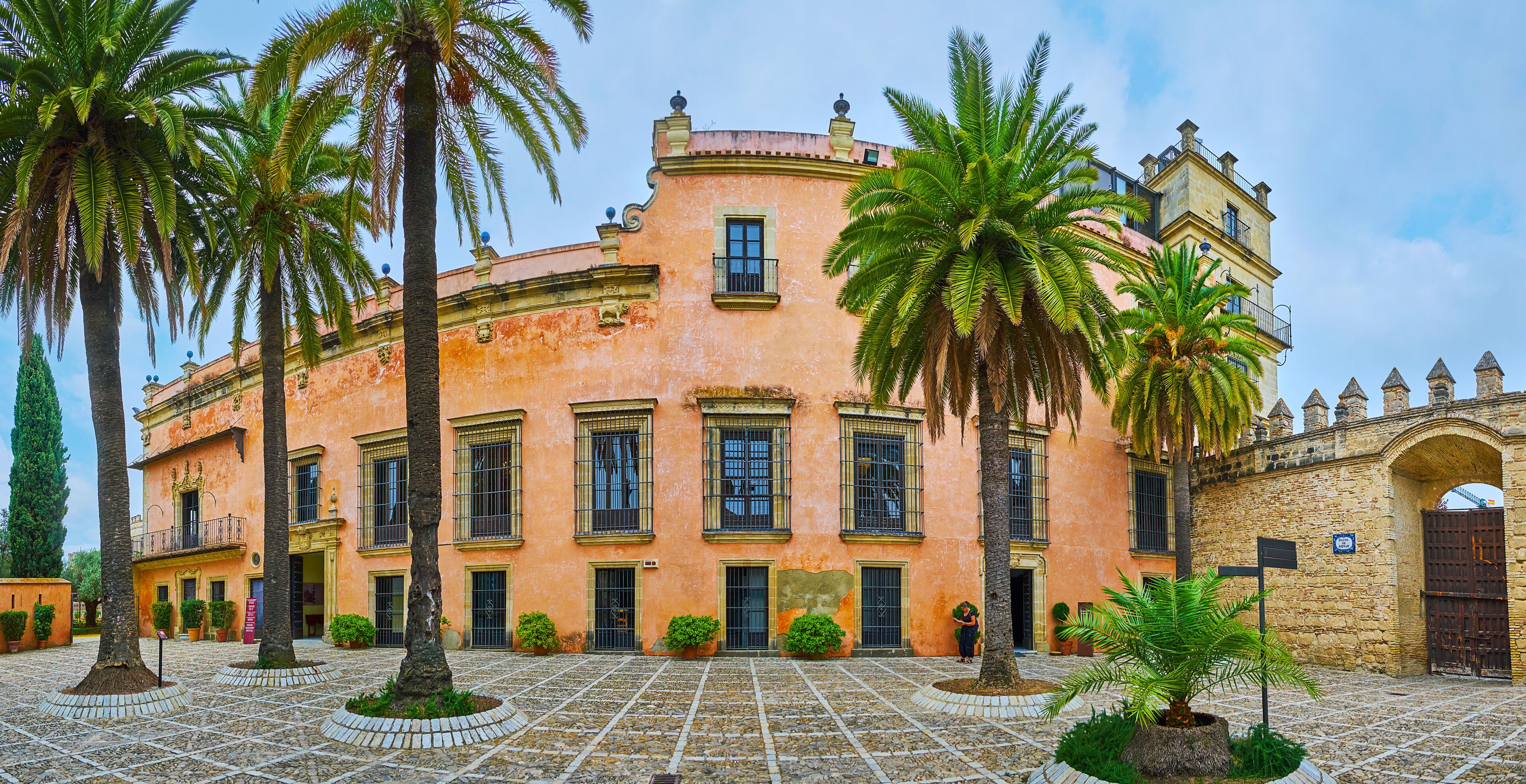 A historic building with a pink facade, palm trees, and a stone archway.