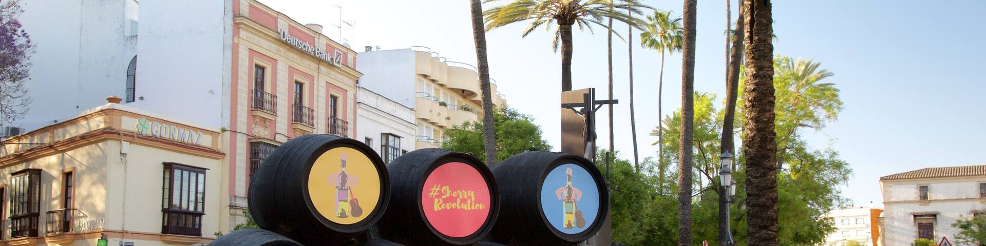 A collection of colorful barrels with various designs and text, placed on a street with palm trees and buildings in the background.