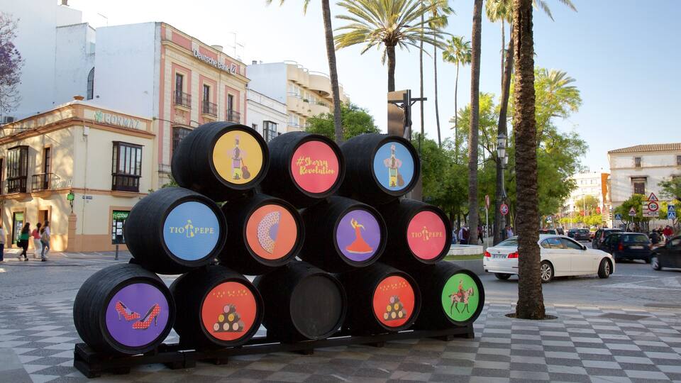A collection of colorful barrels with various designs and text, placed on a street with palm trees and buildings in the background.